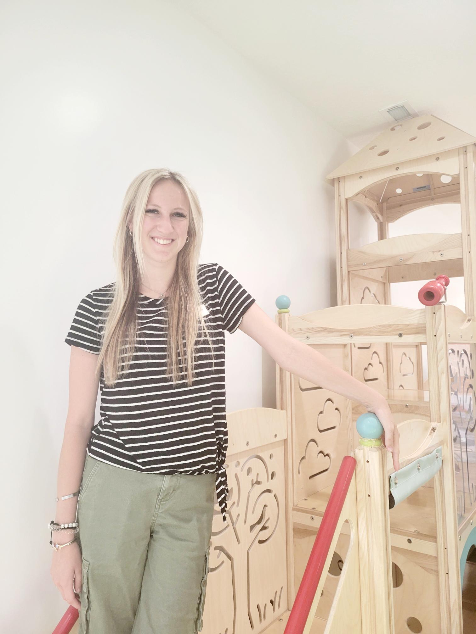 Riley wearing a black and white stripped shirt and olive green pants leaning against a large wooden jungle gym