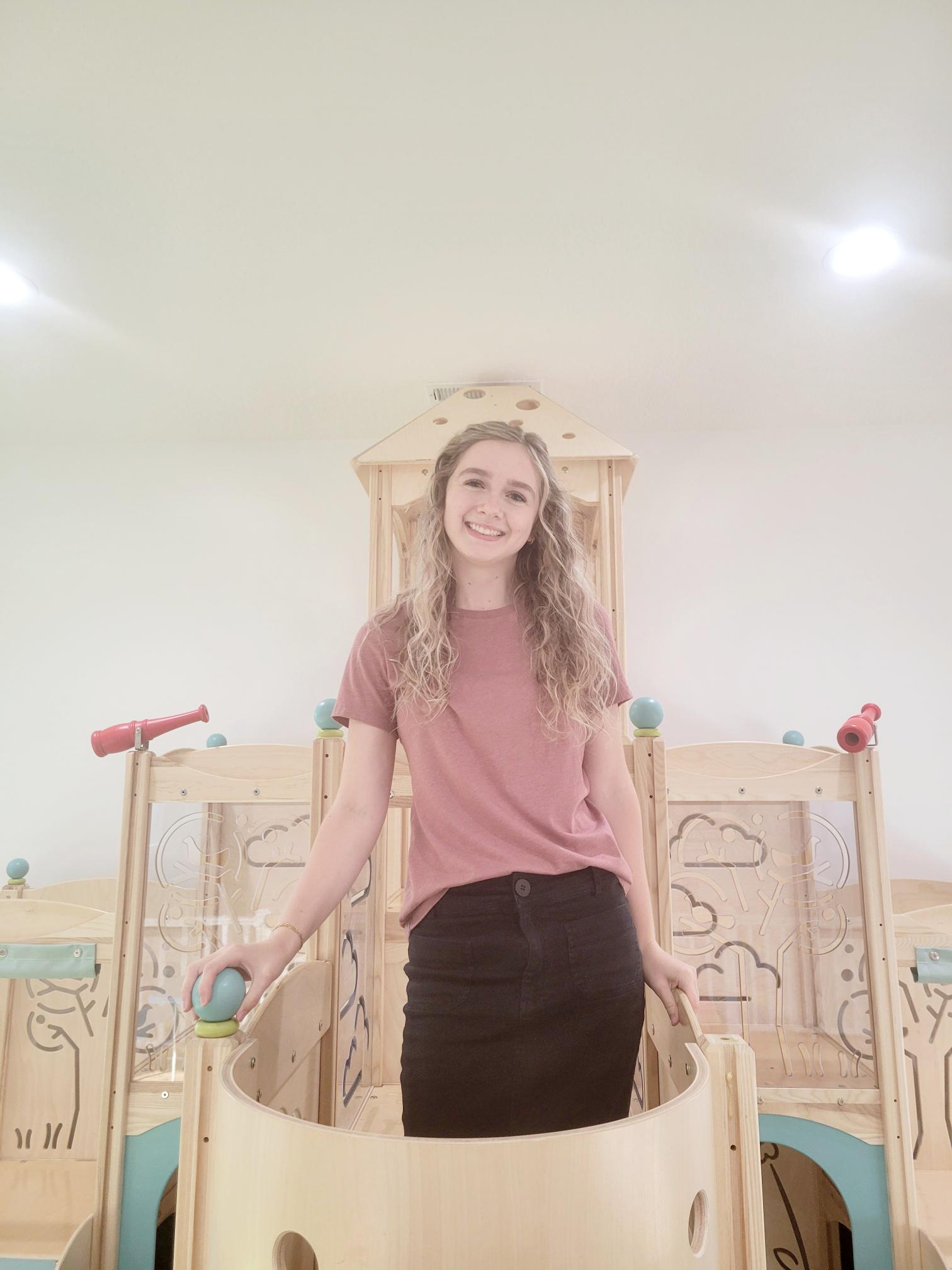 Sierra wearing a pink t-shirt and black pants standing on a wooden jungle gym platform